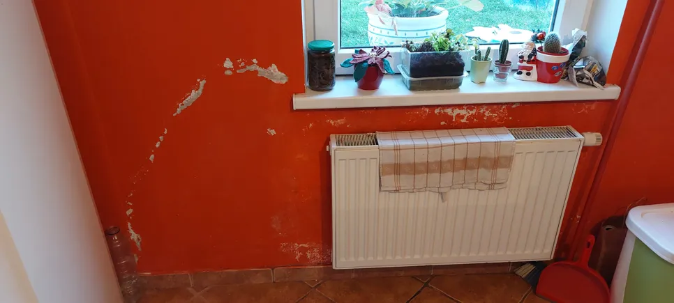 Peeling paint on an orange wall shows possible water damage or humidity issues near a radiator.