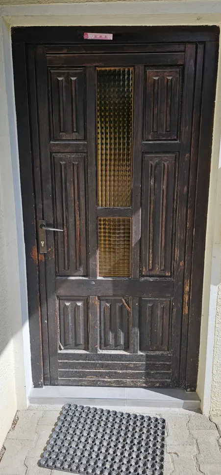 A worn wooden front door with peeling paint and a textured glass panel, showing signs of weathering.