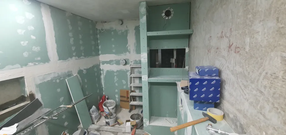 Obnova kopalnice v teku, prikazuje nedokončane zelene suhomontažne panele z dodatki in orodjem raztresenim okoli.