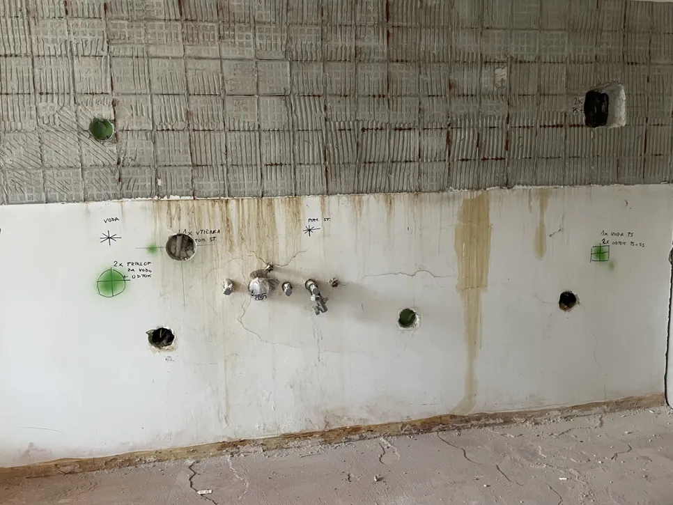 Stena kopalnice z razkritimi vodovodnimi cevmi in oznakami za povezave cevi, kar kaže na potek del.