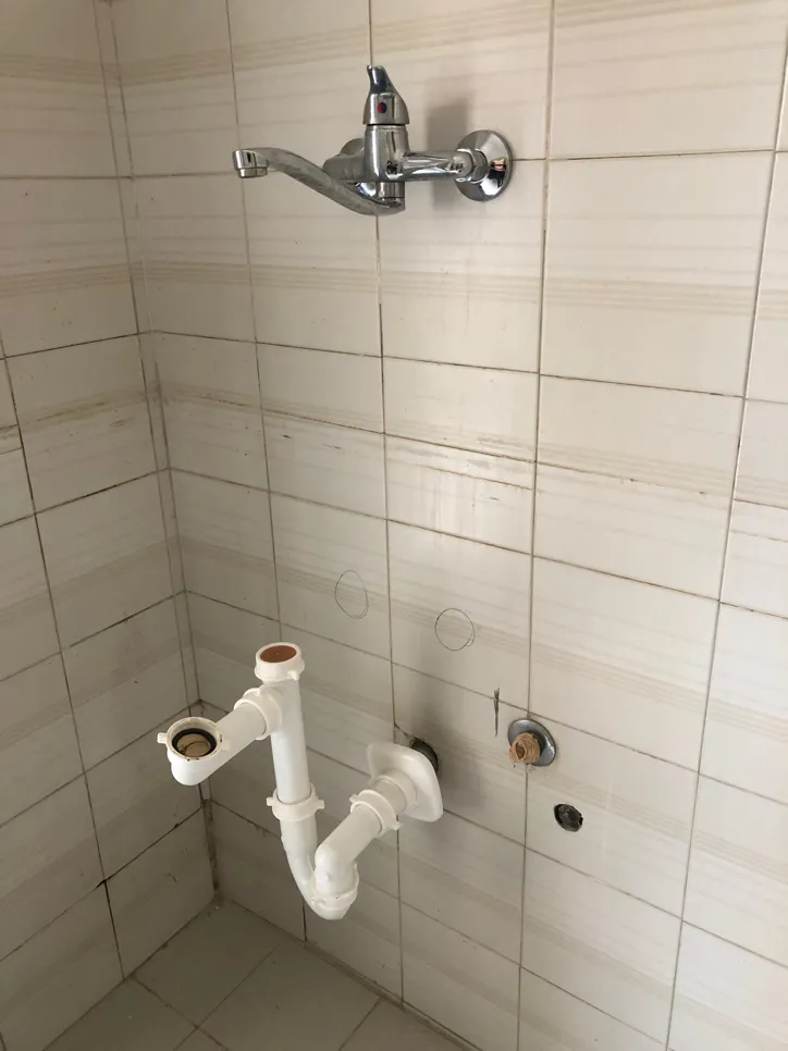 Nedokončana namestitev vodovodnih instalacij v kopalnici, ki prikazuje izpostavljene cevi in pipo na ploščicah.