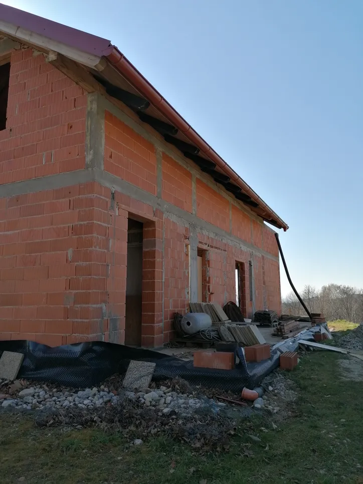 Unfinished brick house with incomplete roofing and siding, showcasing open areas and construction materials nearby.