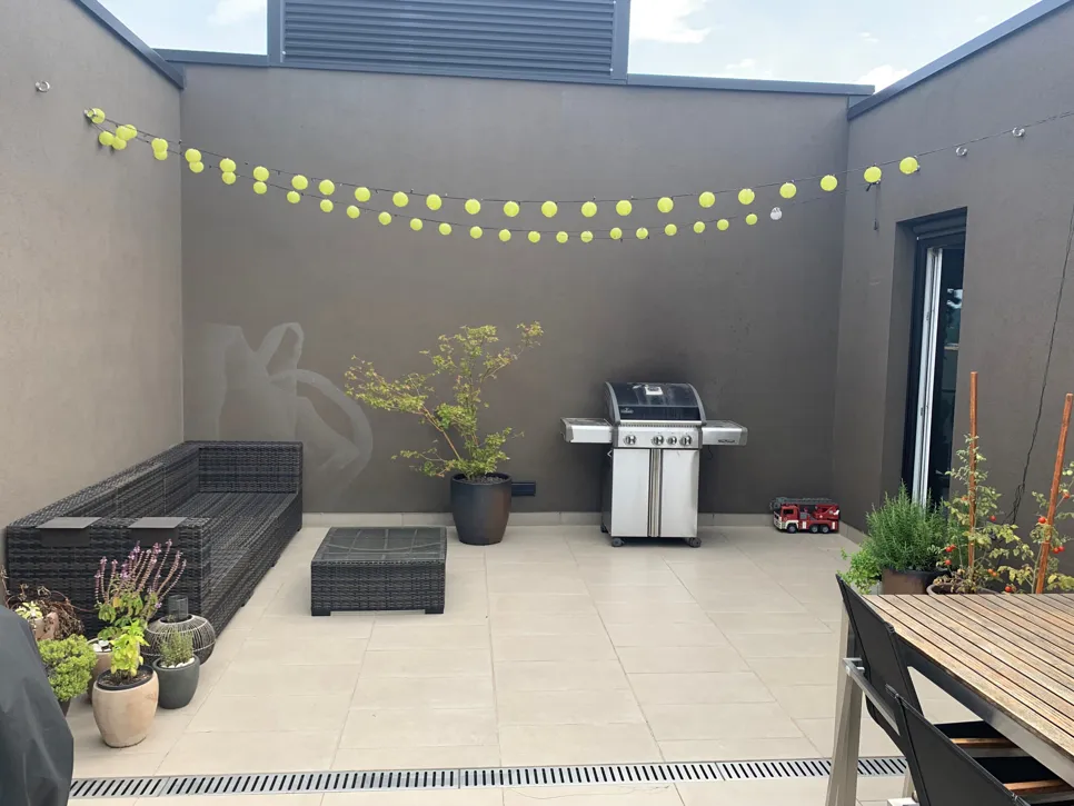 Zunanja terasa z elegantnim žarom, modernim pletenim pohištvom in dekorativno osvetlitvijo za vzdušje.