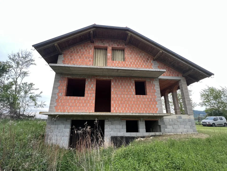 Unfinished brick house with exposed structure and open window spaces, situated in a grassy area.