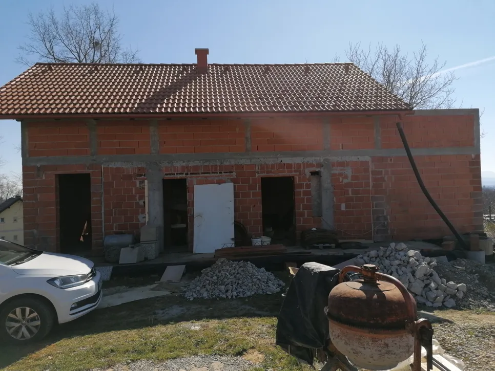 Unfinished brick house with exposed walls and roof tiles, needing further structural completion.