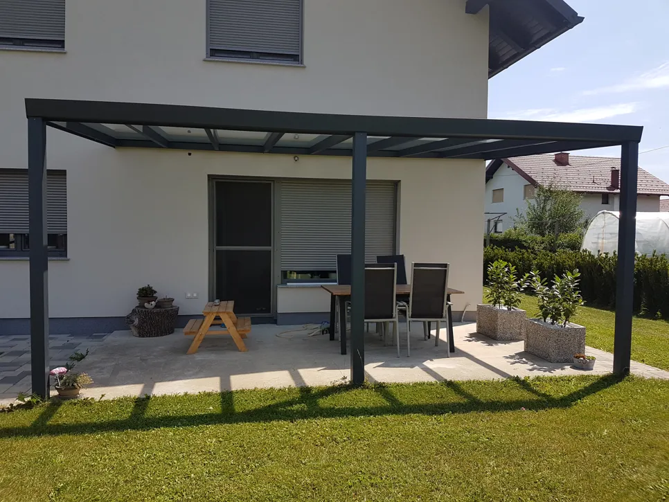 Sodobna kovinska pergola nad teraso z zunanjim pohištvom in živahnimi vrtnimi okolji.