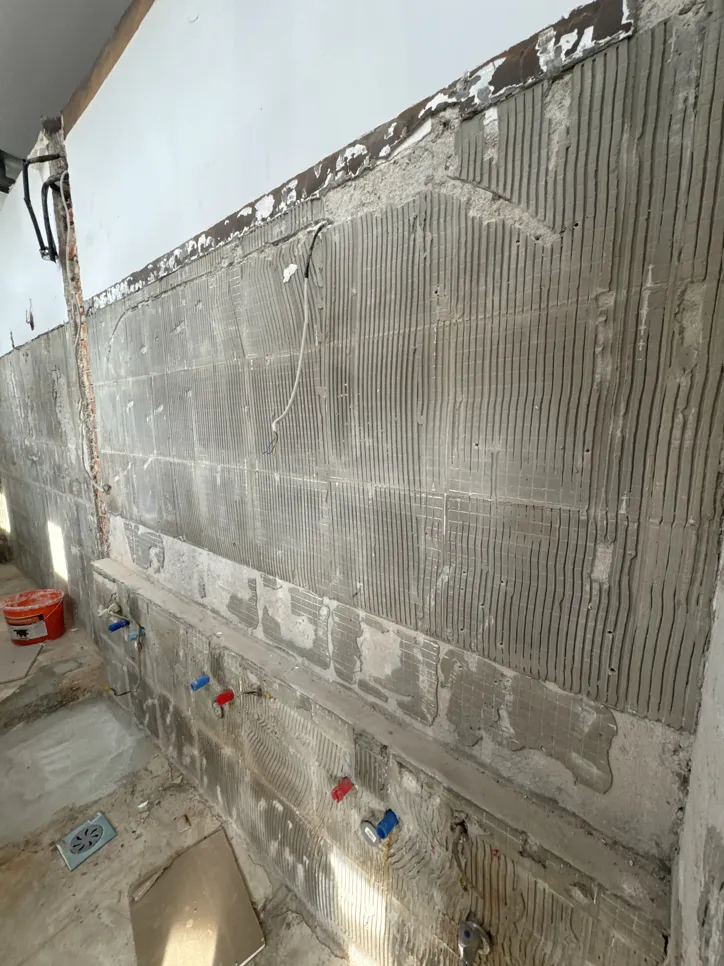 Izpostavljena stena kopalnice s cevmi in lepilnimi utori, pripravljena za namestitev ploščic.