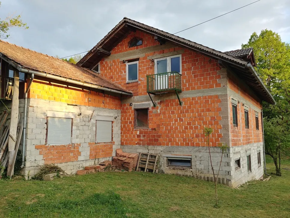 Delno zgrajena opečna hiša z razkrinkano zunanjostjo, ki prikazuje nedokončane stene in okenske okvirje.