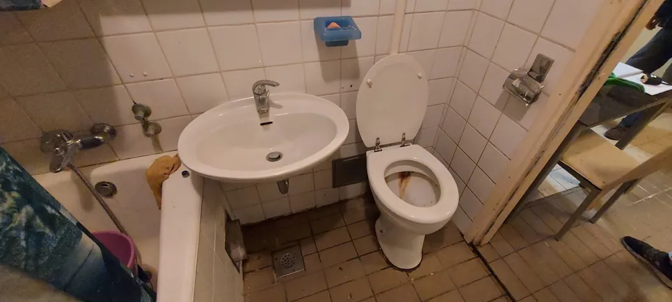 Kompaktna kopalnica z umivalnikom in straniščem v bližini, ki poudarja omejen prostor in nered.