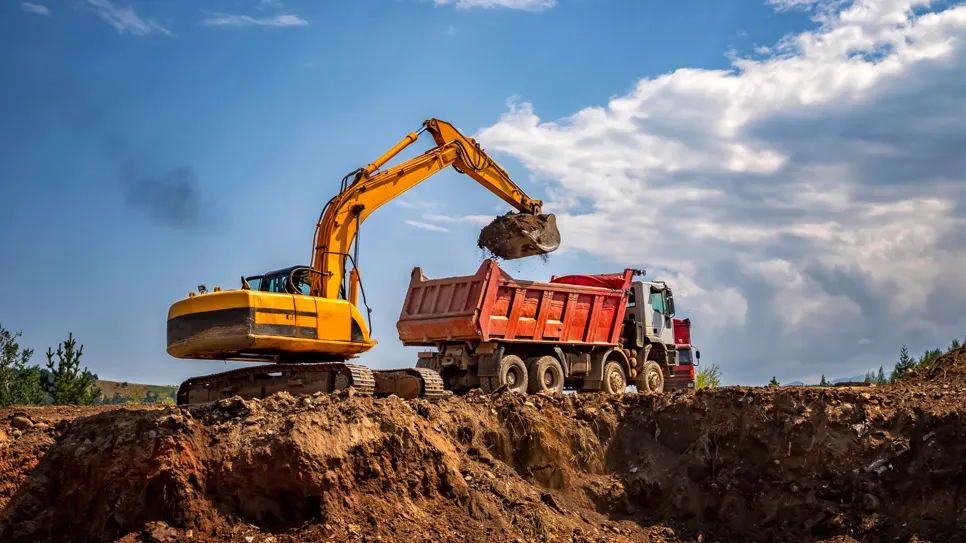 Rumeni bagger prenaša zemljo v rdeči tovornjak na gradbišču.